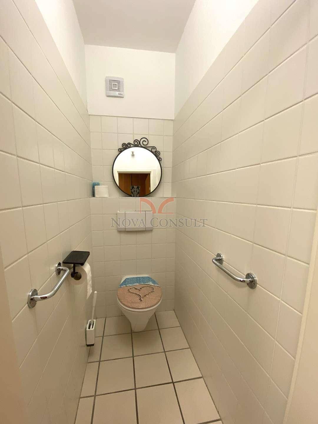 Separate Toilette mit Fliesen, Spiegel und Haltegriffen für Barrierefreiheit.
