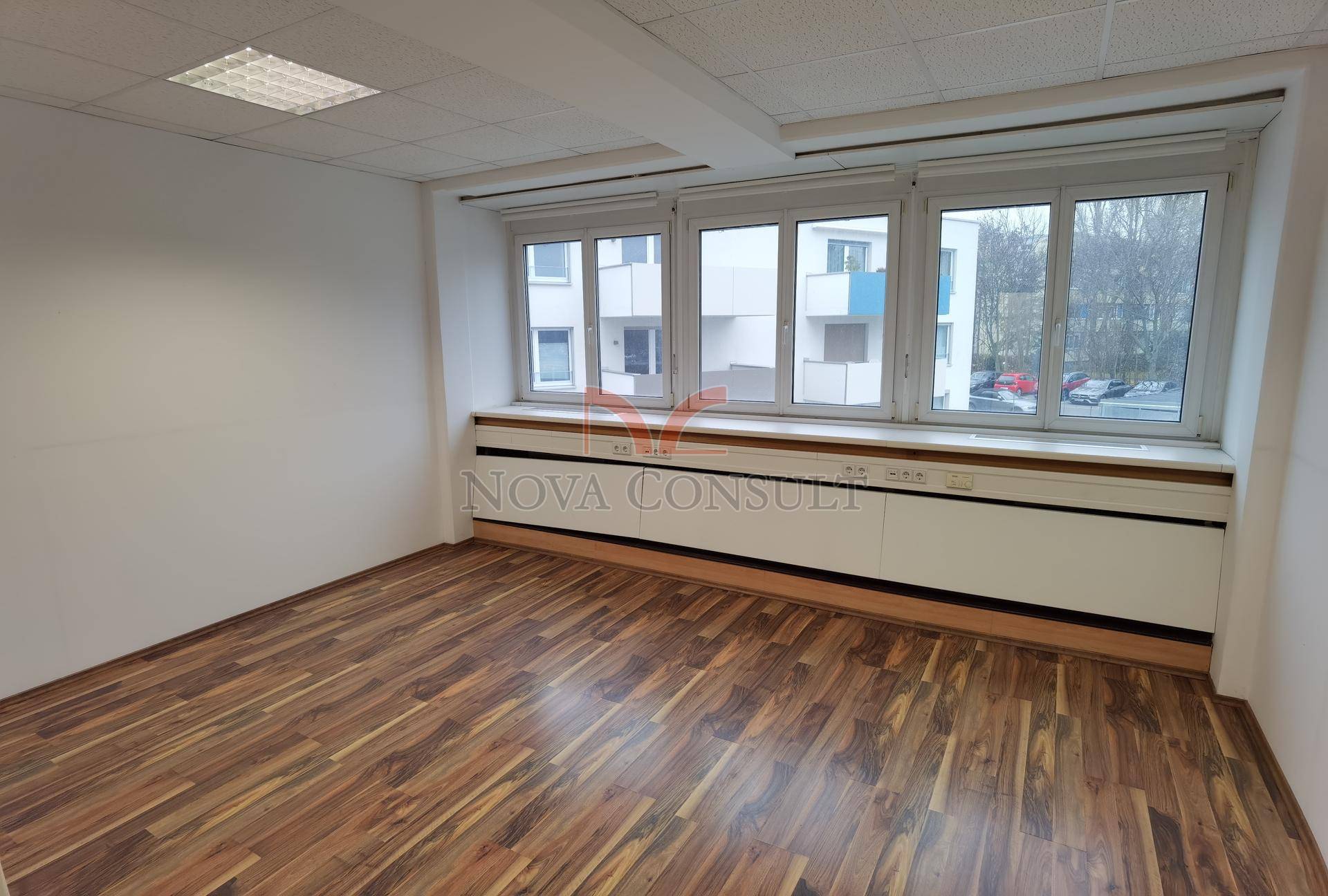 Büro mit großen Fenstern, die einen Blick auf die umliegenden Gebäude und viel Tageslicht bieten.