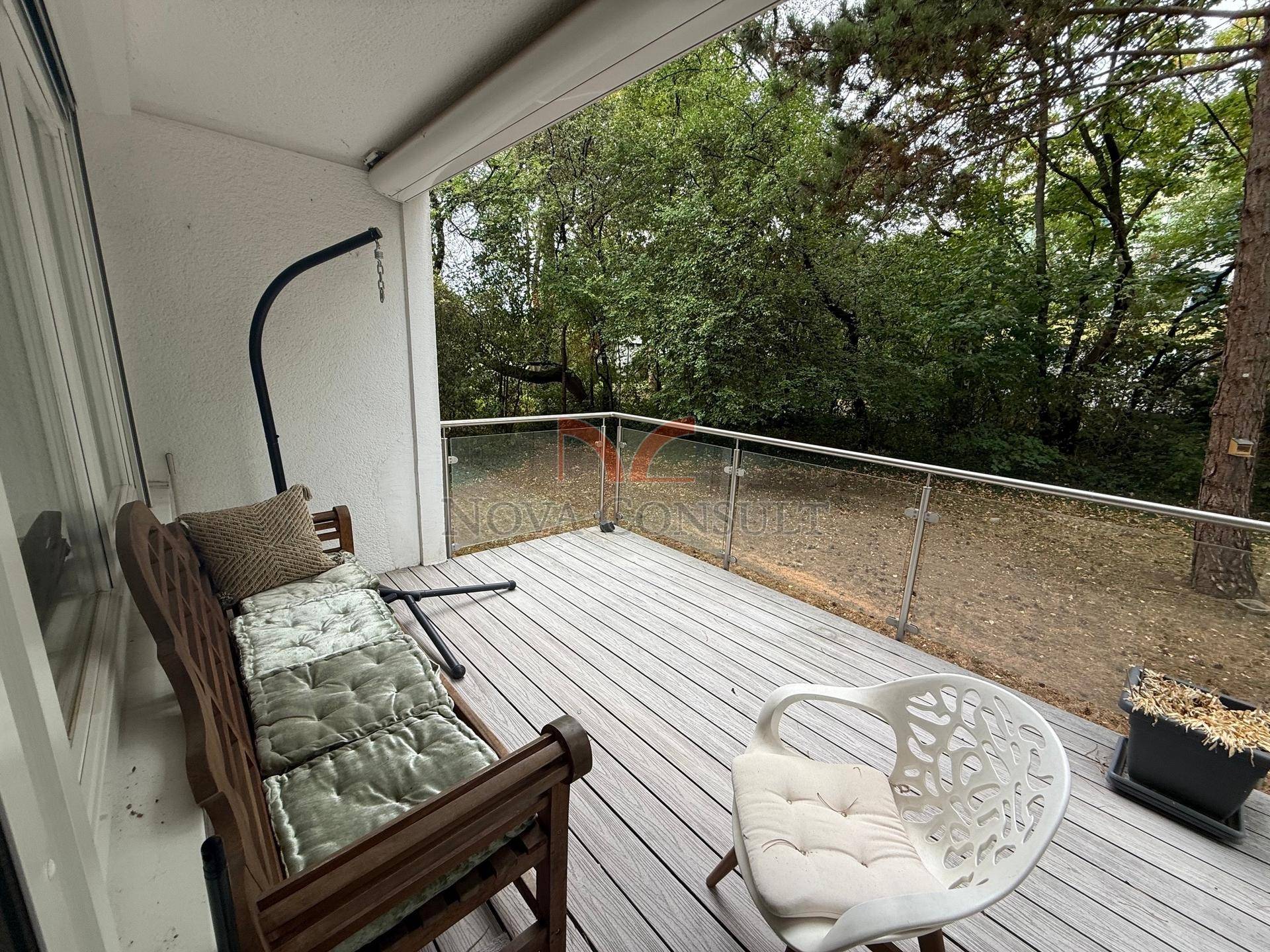 Gemütliche Terrasse mit Holzboden und Glasgeländer, umgeben von Bäumen für Privatsphäre.