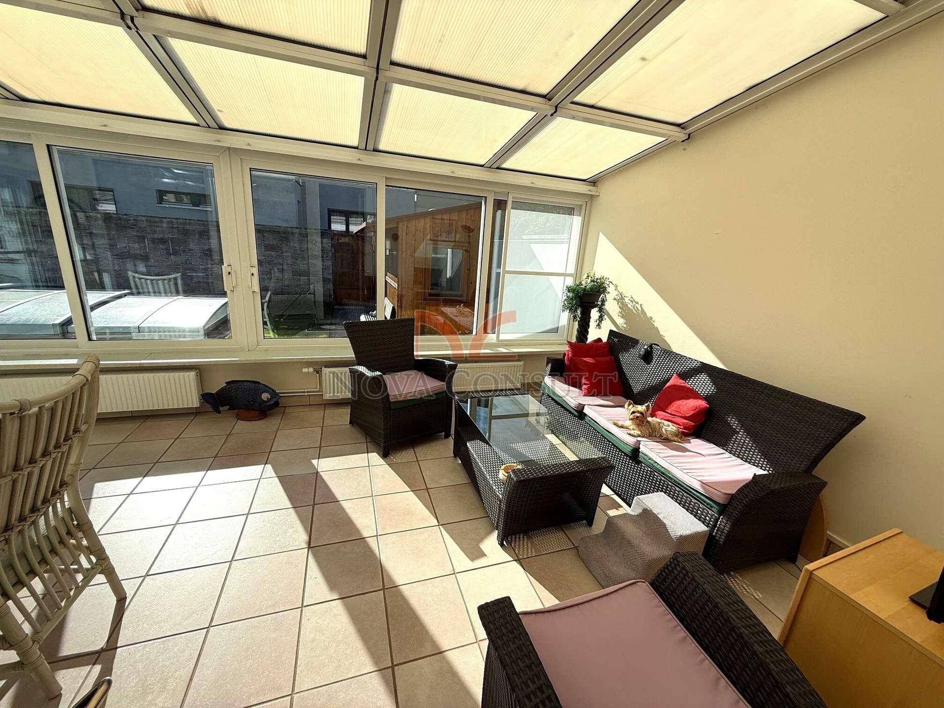 Gemütlicher Lounge-Bereich im Wintergarten mit Rattanmöbeln und Blick ins Grüne.