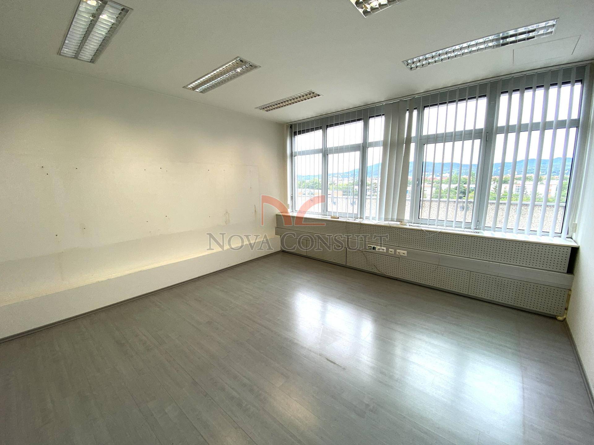 Helles, leeres Bürozimmer mit einer Fensterfront, die für viel Tageslicht sorgt.