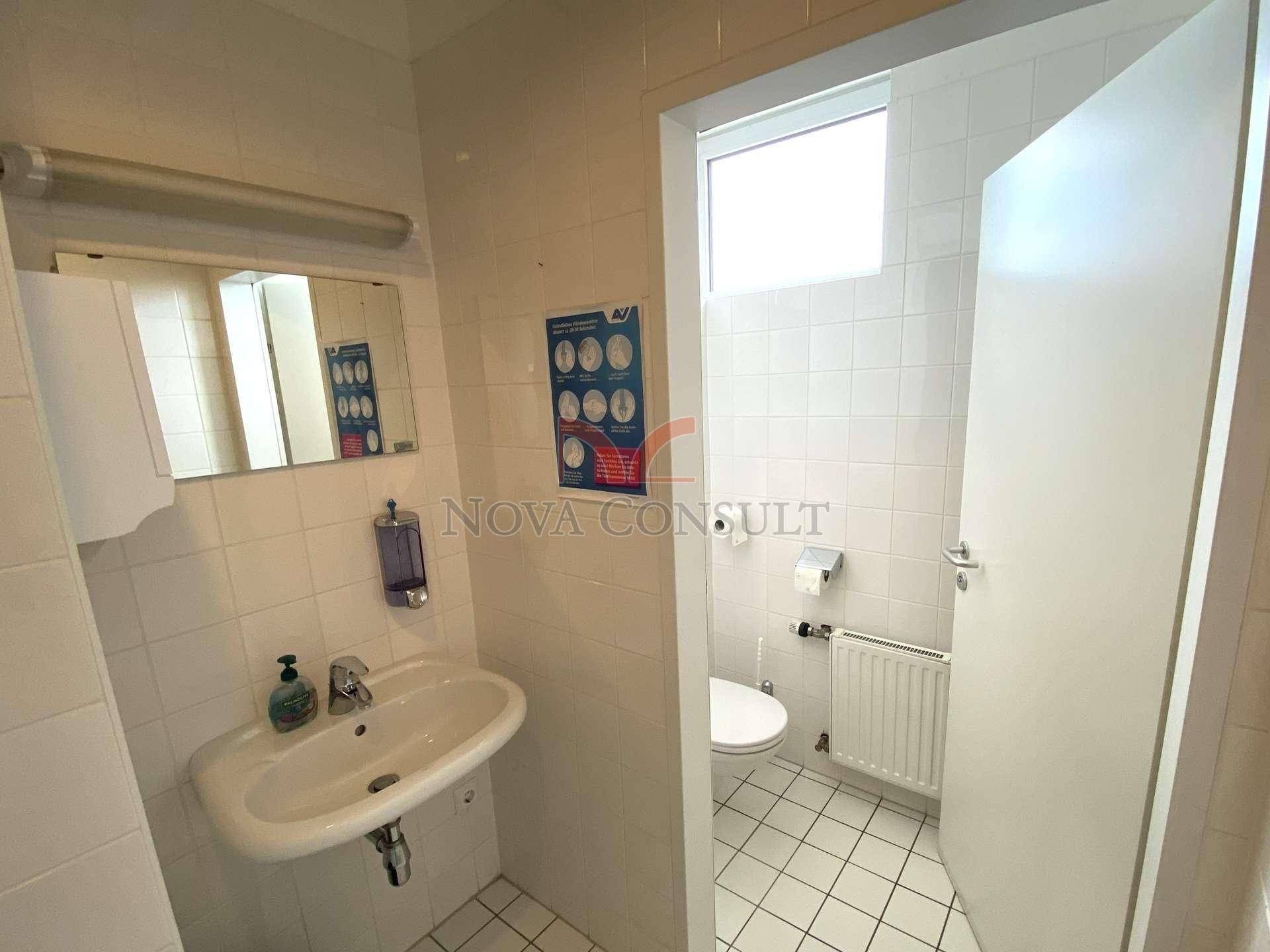 Gefliestes WC mit Waschbecken und separater Toilettenkabine, ausgestattet mit einem Fenster.