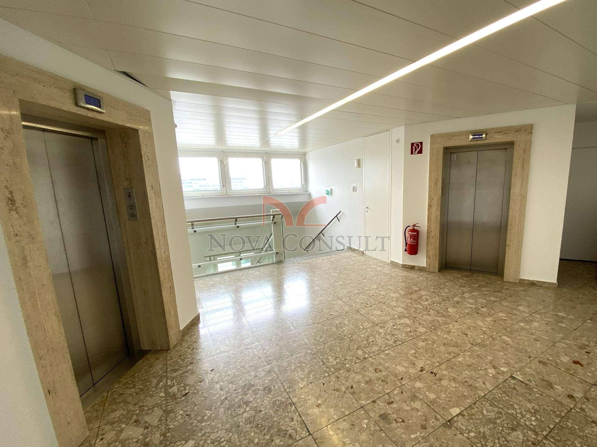 Heller Flurbereich mit zwei Aufzügen, Treppenhaus und Terrazzoboden.
