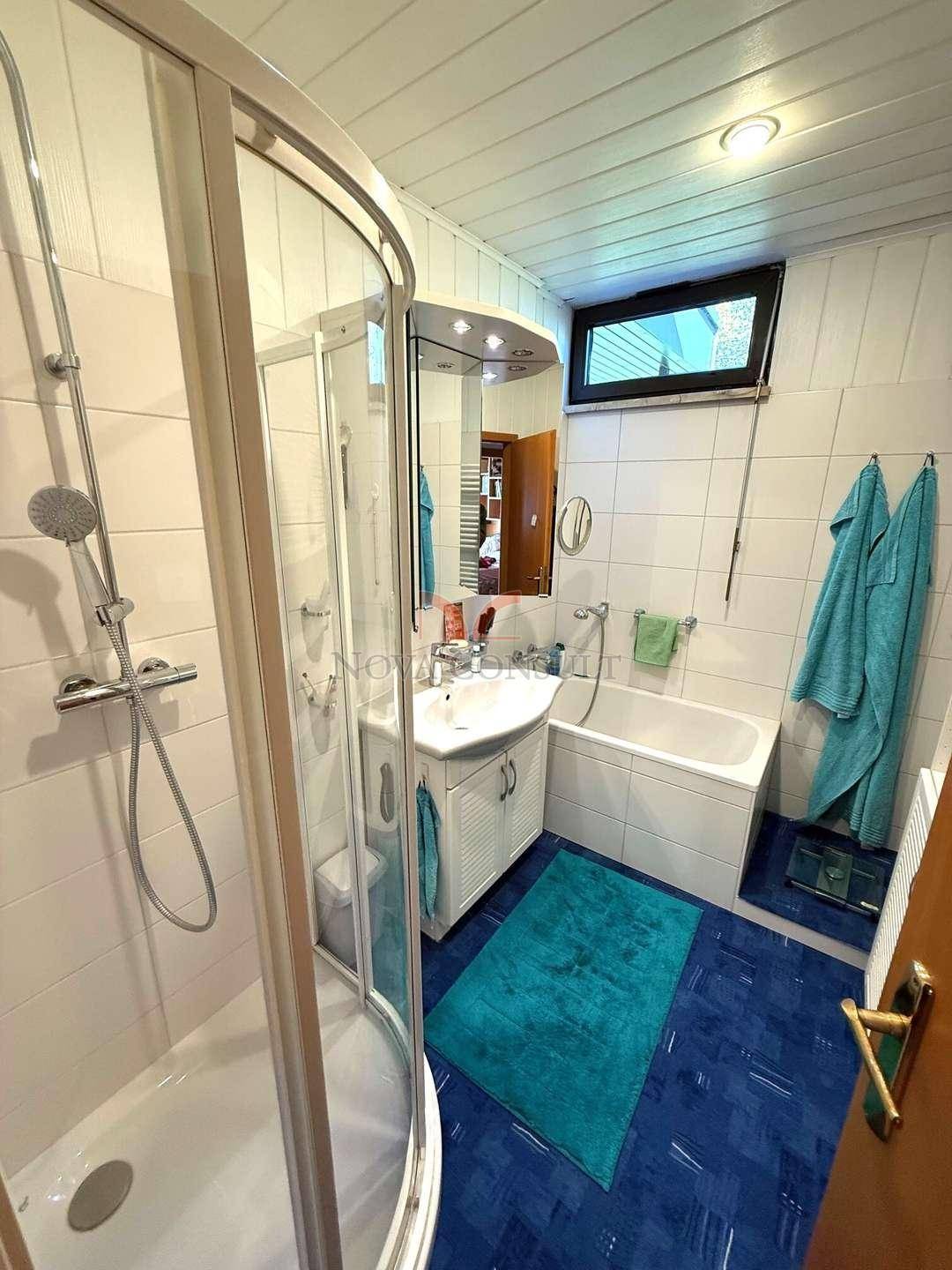 Badezimmer mit Duschkabine, Badewanne, Waschbecken und blauen Fliesen.