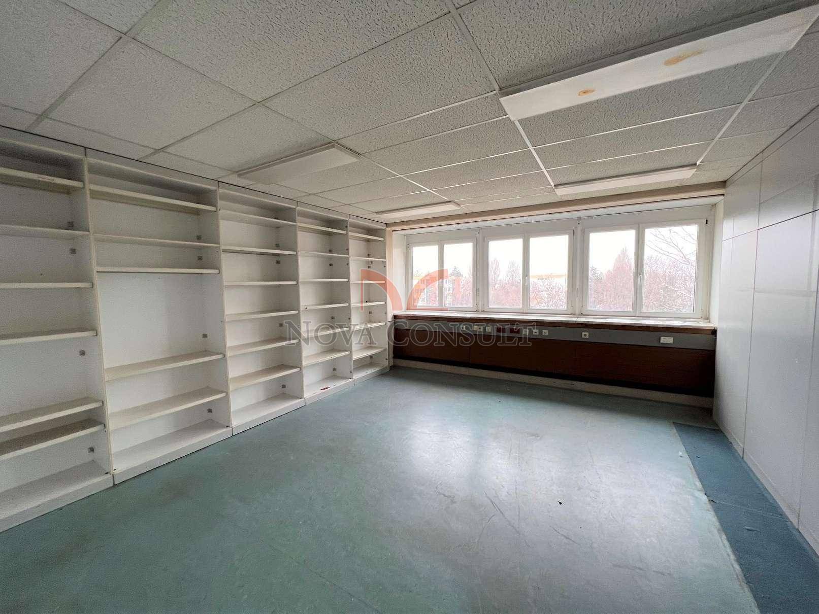 Leeres Büro mit eingebauten Regalen entlang einer Wand und großen Fenstern für viel Helligkeit.