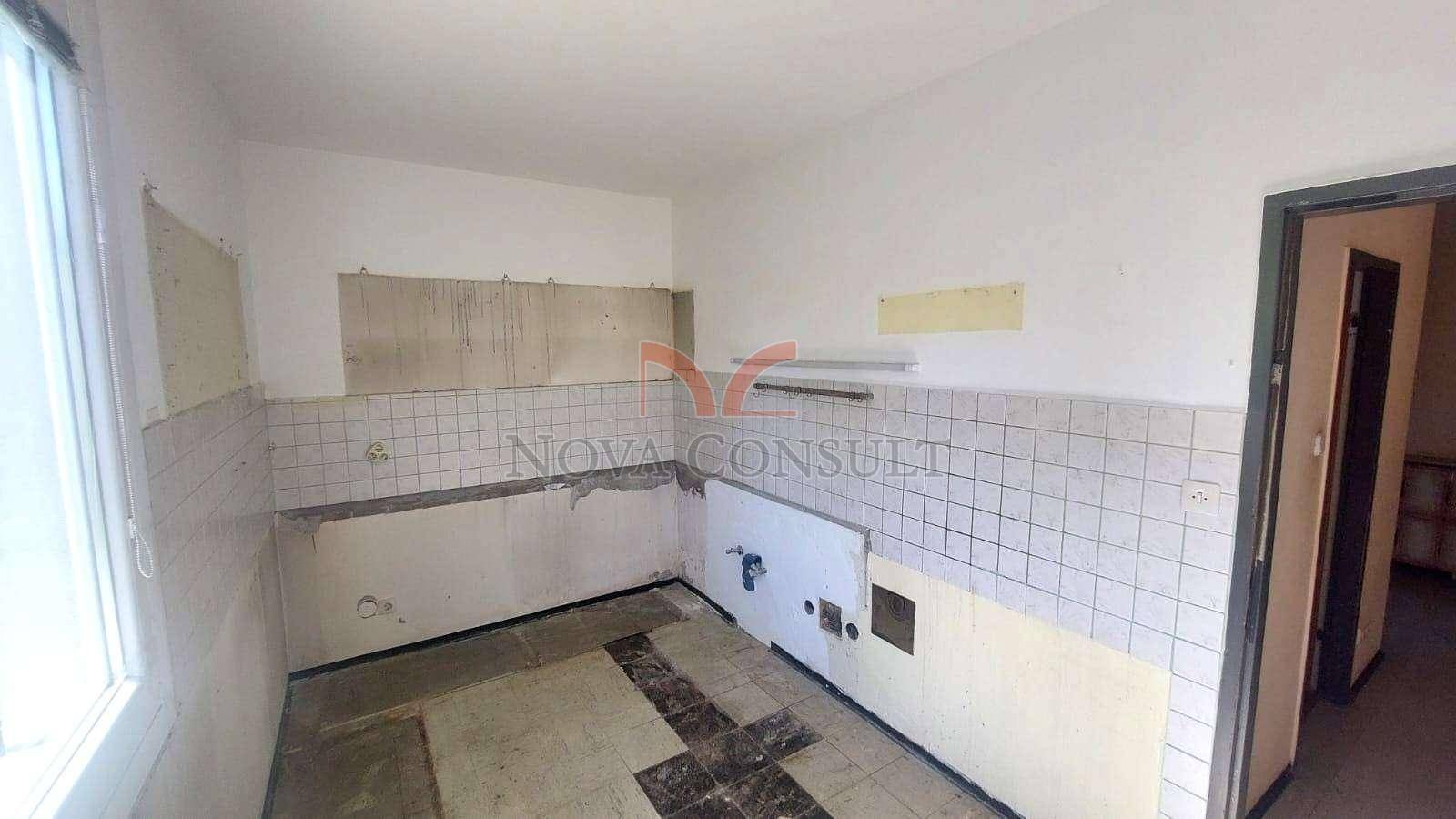 Leere Küche mit alten Fliesen und Fenster, bereit für eine komplette Neugestaltung.