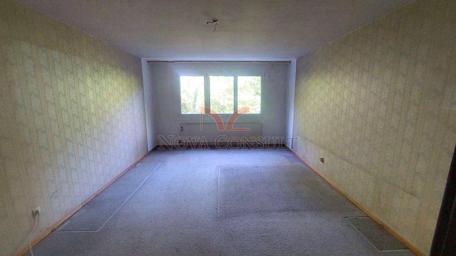 Leeres Zimmer mit Teppichboden und einem Fenster, das Tageslicht hereinlässt.