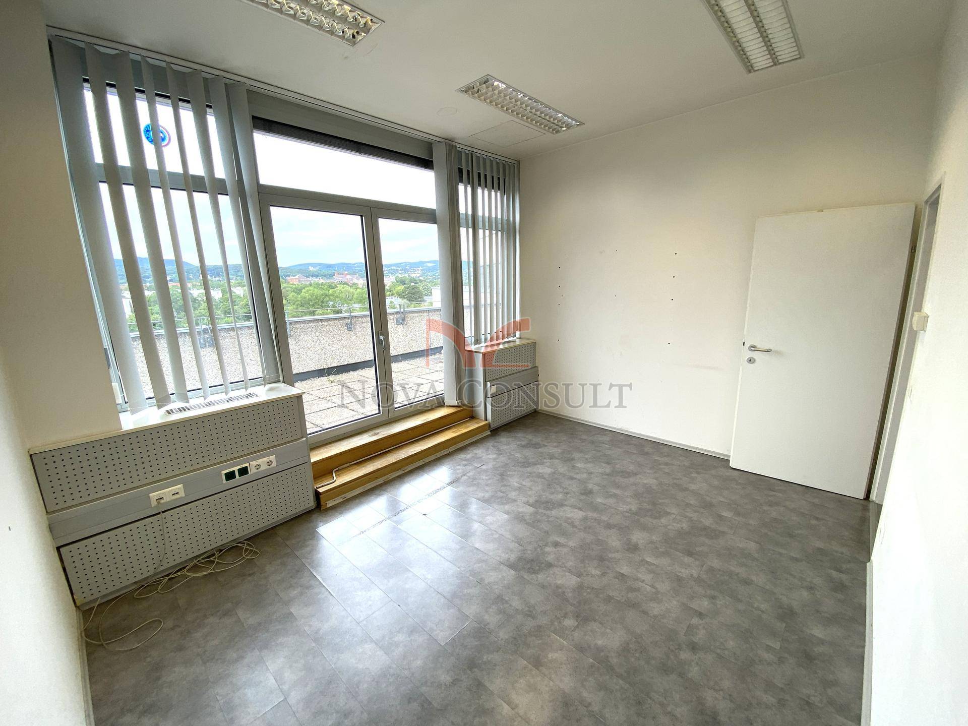 Leeres Bürozimmer mit großen Fenstern und direktem Zugang zu einem Außenbereich.