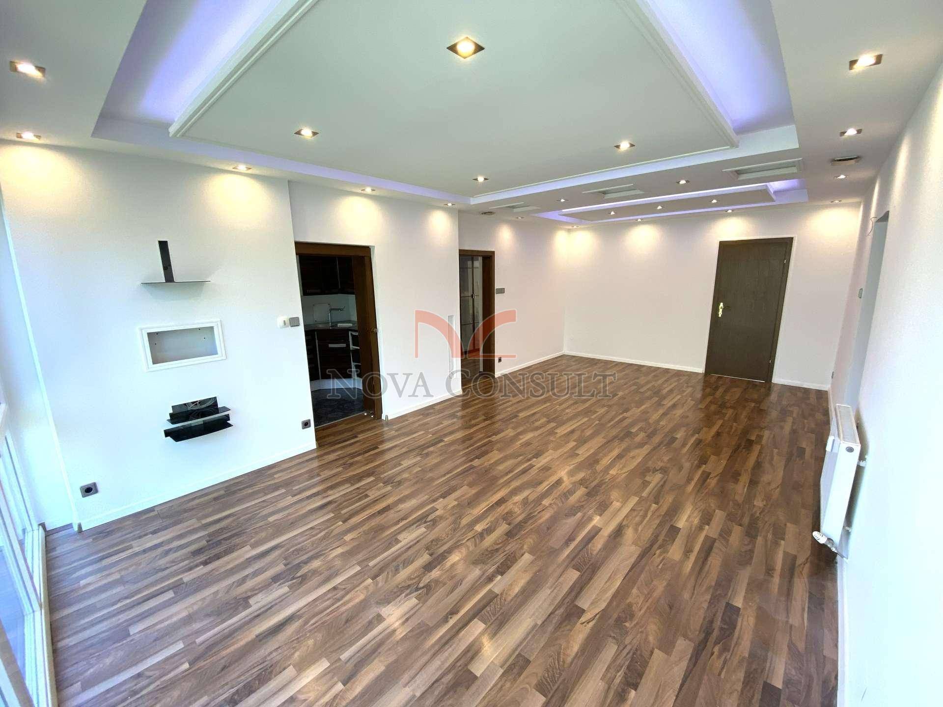 Helles Wohnzimmer mit elegantem Deckenlichtdesign, Holzboden und weißen Wänden.