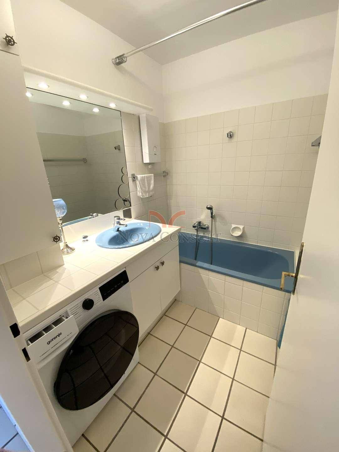 Badezimmer mit Badewanne, Waschbecken und Waschmaschine, gefliesten Wänden und Boden.