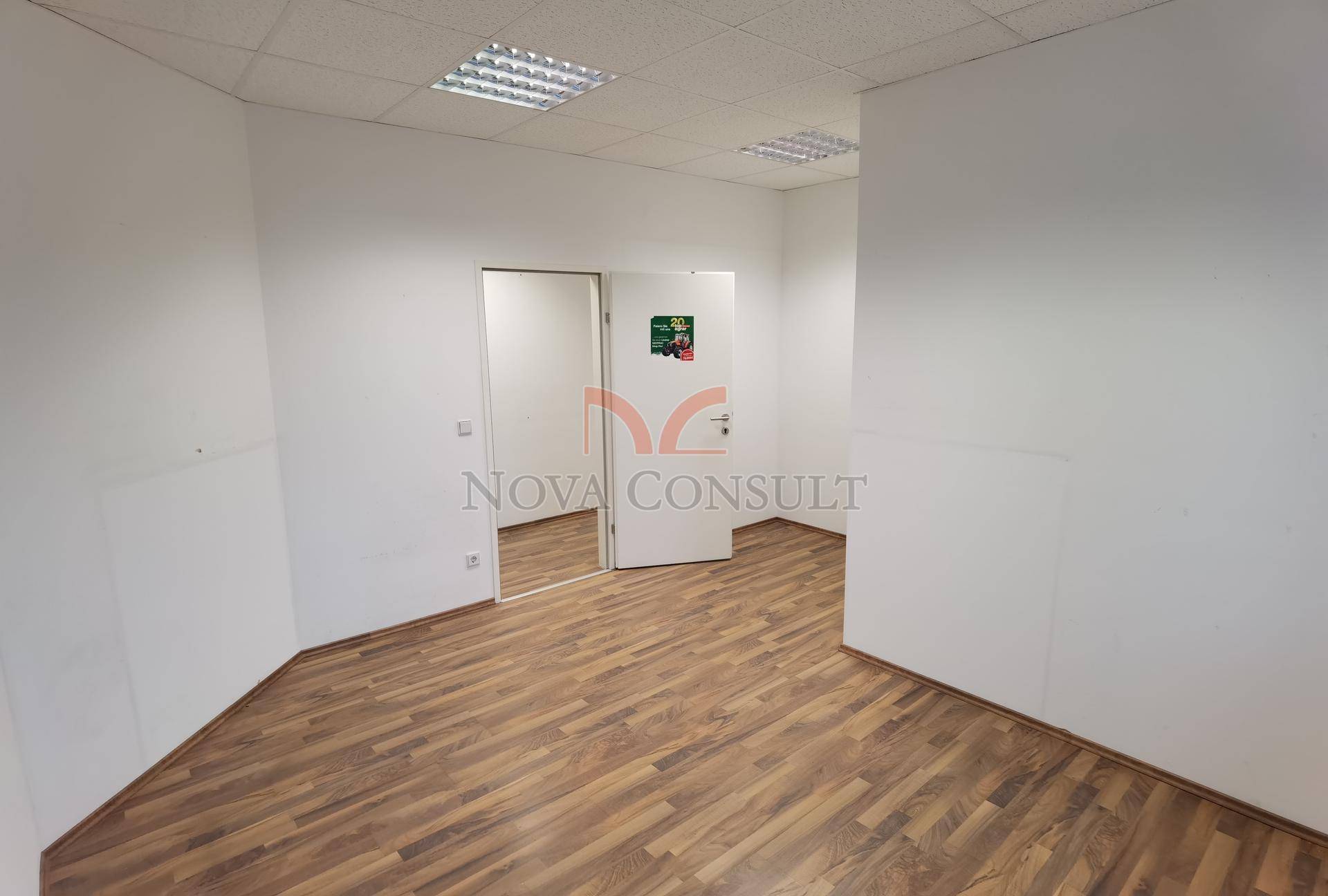 Leeres Büro mit Holzboden und weißen Wänden, das durch zwei offene Türen mit angrenzenden Räumen verbunden ist.