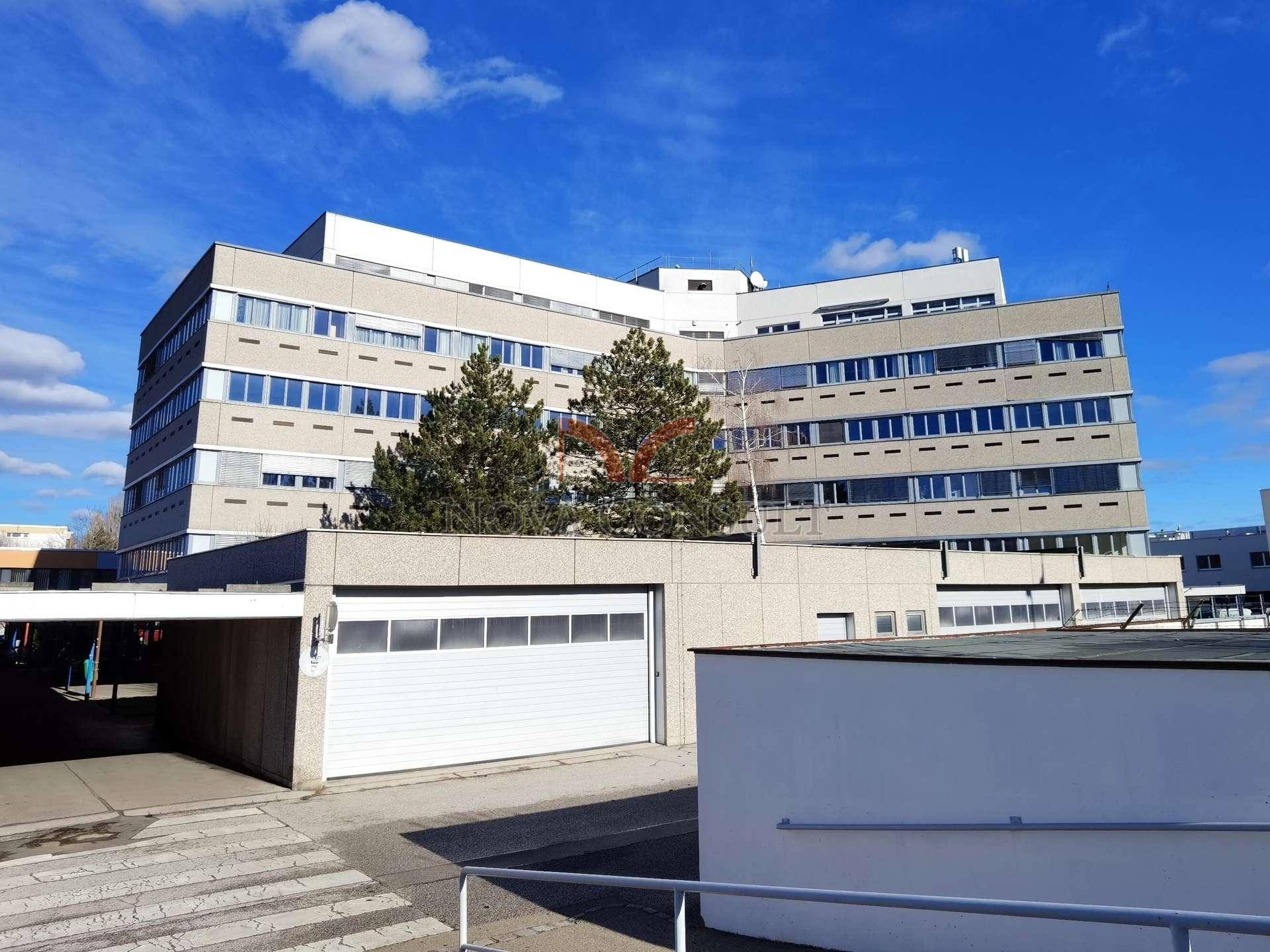 Großes Gebäude mit einer Garageneinfahrt im Vordergrund und Bäumen unter blauem Himmel.