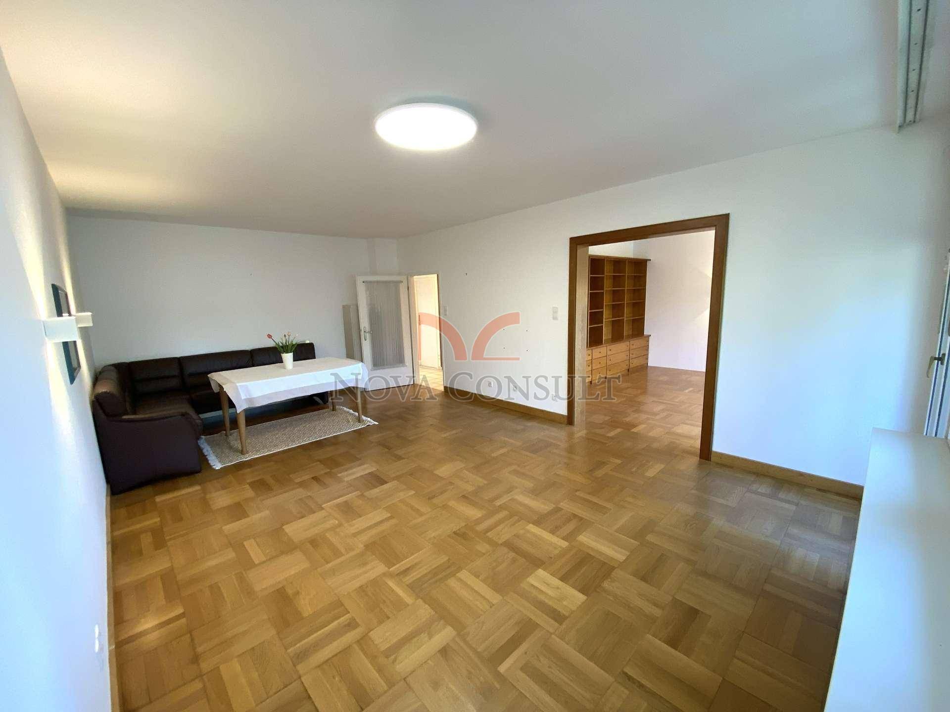 Heller Wohnbereich mit Parkettboden, Sofa und Blick in ein angrenzendes Zimmer.