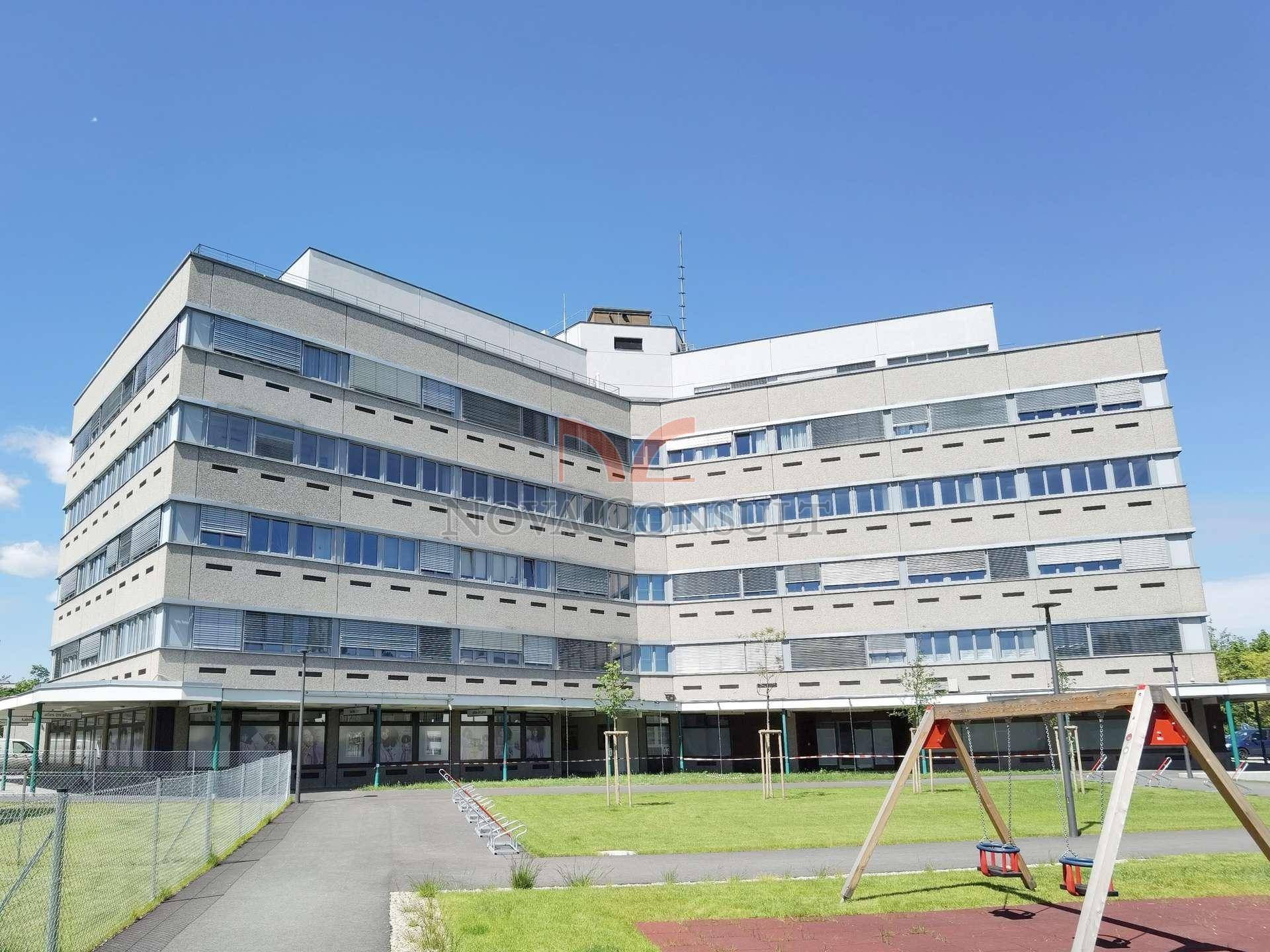 Großes Gebäude mit vielen Fenstern und einem Spielplatz im Vordergrund unter klarem Himmel.