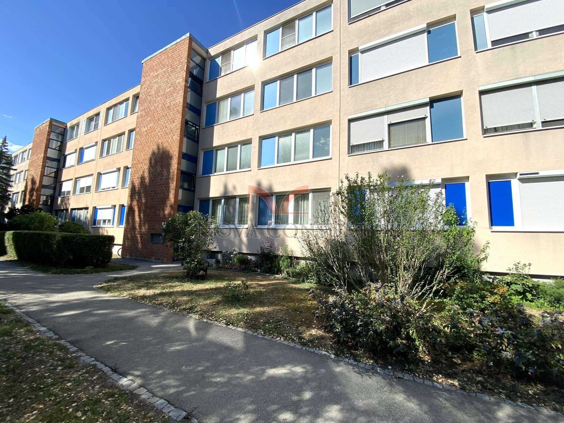 Mehrfamilienhaus mit moderner Fassade, vielen Fenstern und gepflegter Außenanlage.