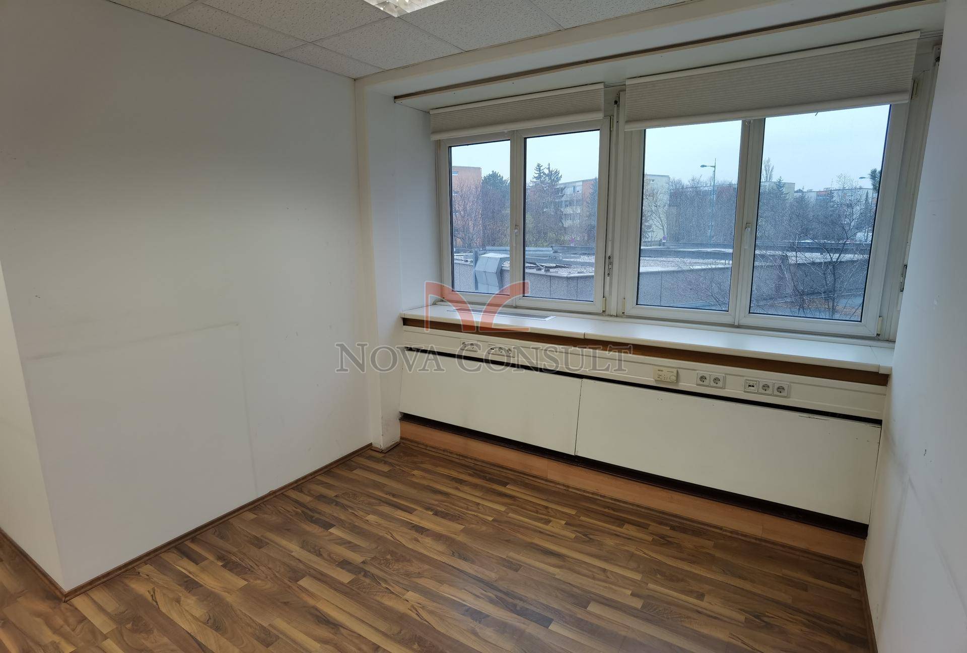Kleineres Büro mit zwei großen Fenstern, die für ausreichend Tageslicht sorgen, und einem warmen Holzboden.