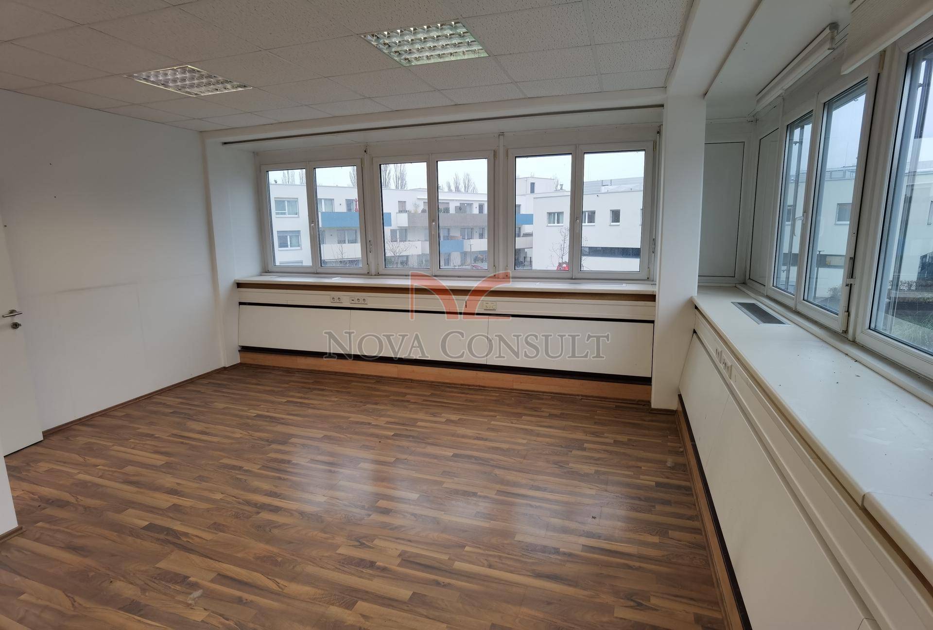 Helles Büro mit Holzboden und Fenstern, die einen Blick auf die Stadtlandschaft bieten.