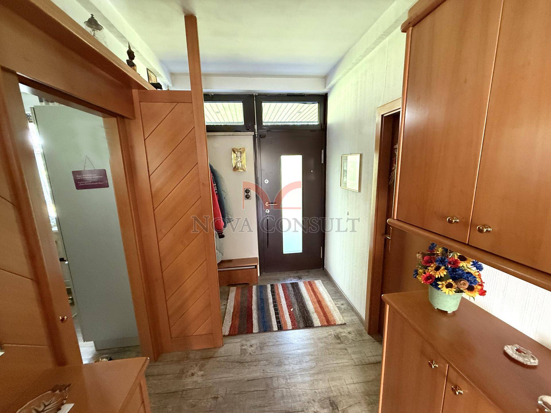 Eingangsbereich mit Garderobe, Holzmöbeln und einem bunten Teppichläufer.