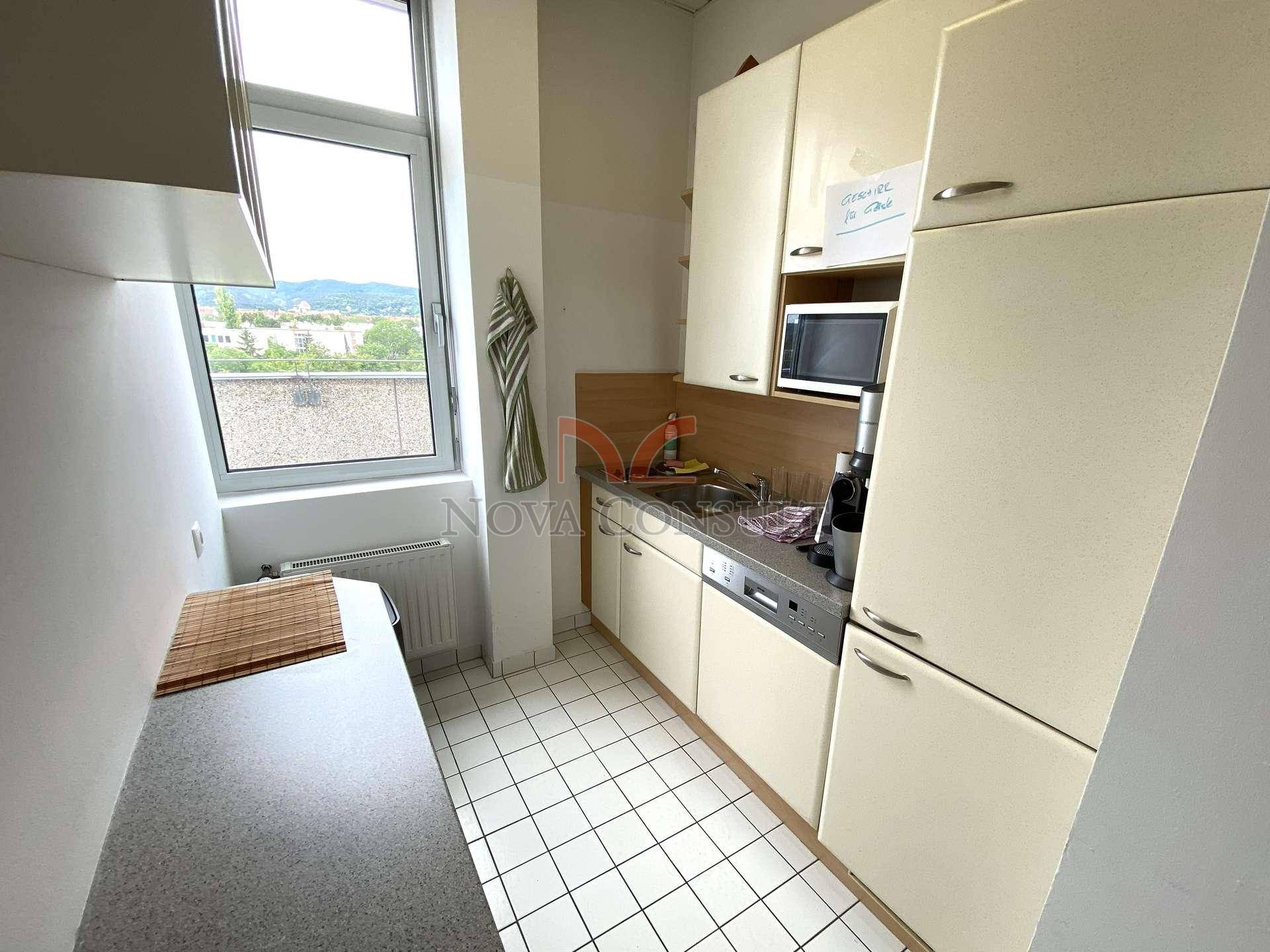 Kleine Einbauküche mit hellen Schränken, Fenster und grundlegenden Küchengeräten.