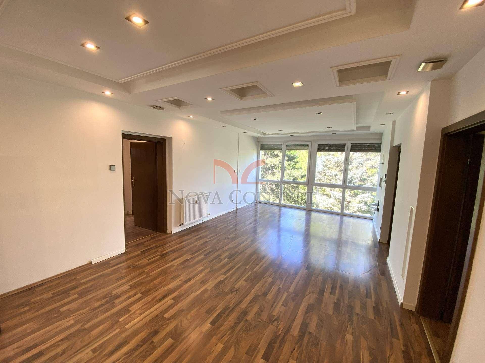 Geräumiges Wohnzimmer mit Holzboden, großen Fenstern und moderner Deckenbeleuchtung.