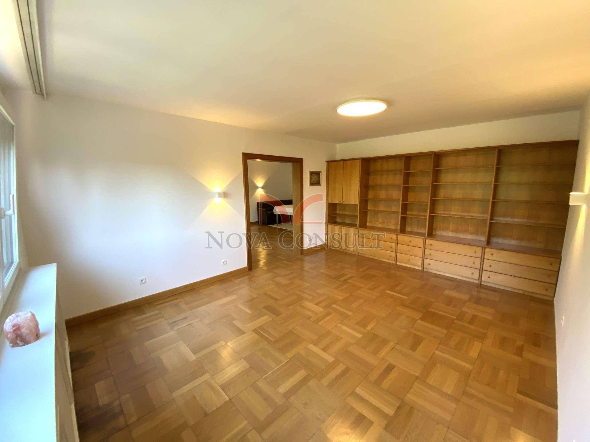 Wohnzimmer mit Einbauregalen, Parkettboden und Blick in ein weiteres Zimmer.