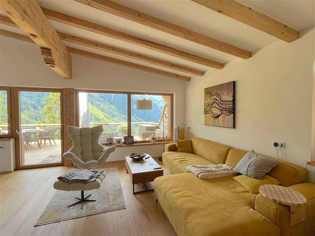 Lichtdurchflutetes Wohnzimmer mit gelbem Sofa, Holzbalken und Panoramablick auf die Berge.