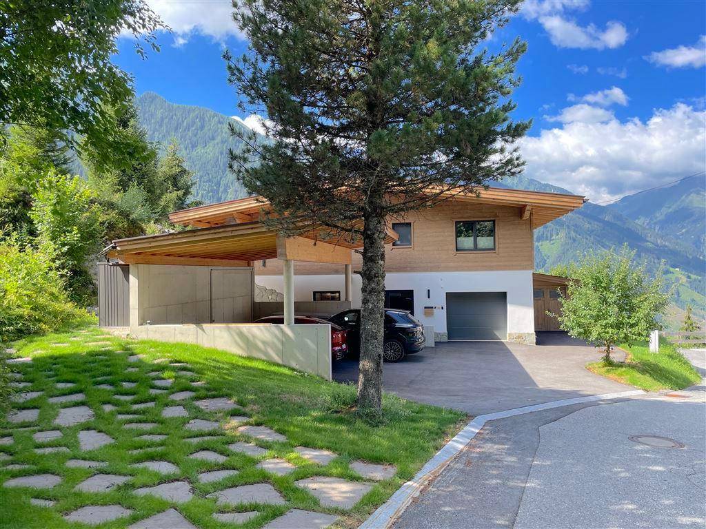 Modernes Einfamilienhaus mit Carport und Garage, umgeben von grüner Natur und Bergen.