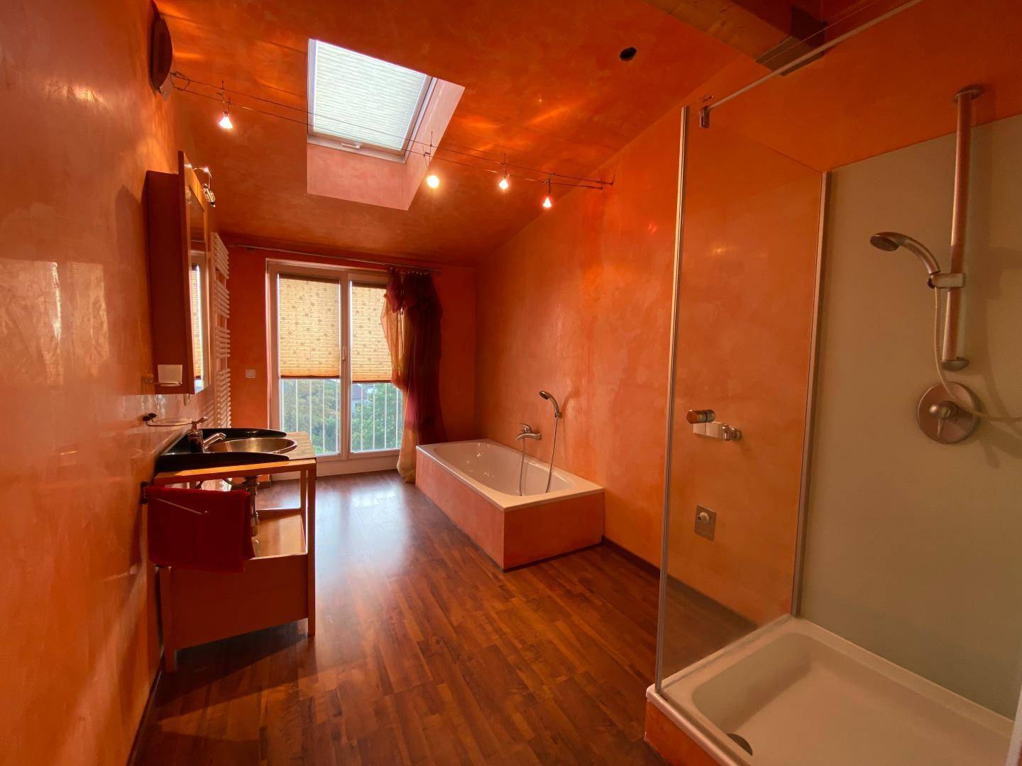 Geräumiges Badezimmer mit orangefarbenen Wänden, Badewanne, Dusche und Dachfenster.