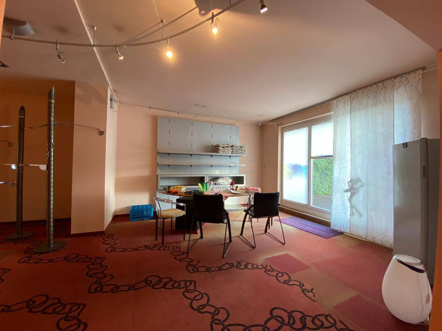 Flexibler Verkaufsraum mit Teppichboden, Regalen und großem Fenster mit Blick ins Grüne.