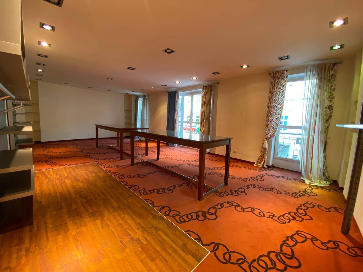 Geräumiger Verkaufsraum mit gemustertem Teppichboden, Holzbodenakzenten und großen Fenstern.