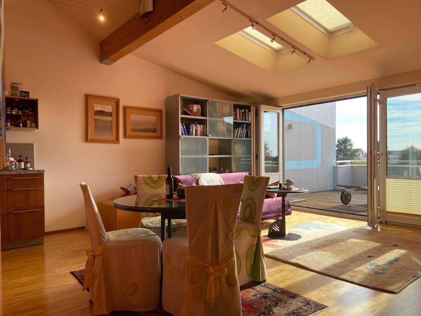 Gemütlicher Wohn-Essbereich mit Holzboden, Dachfenstern und Zugang zu einer Terrasse.