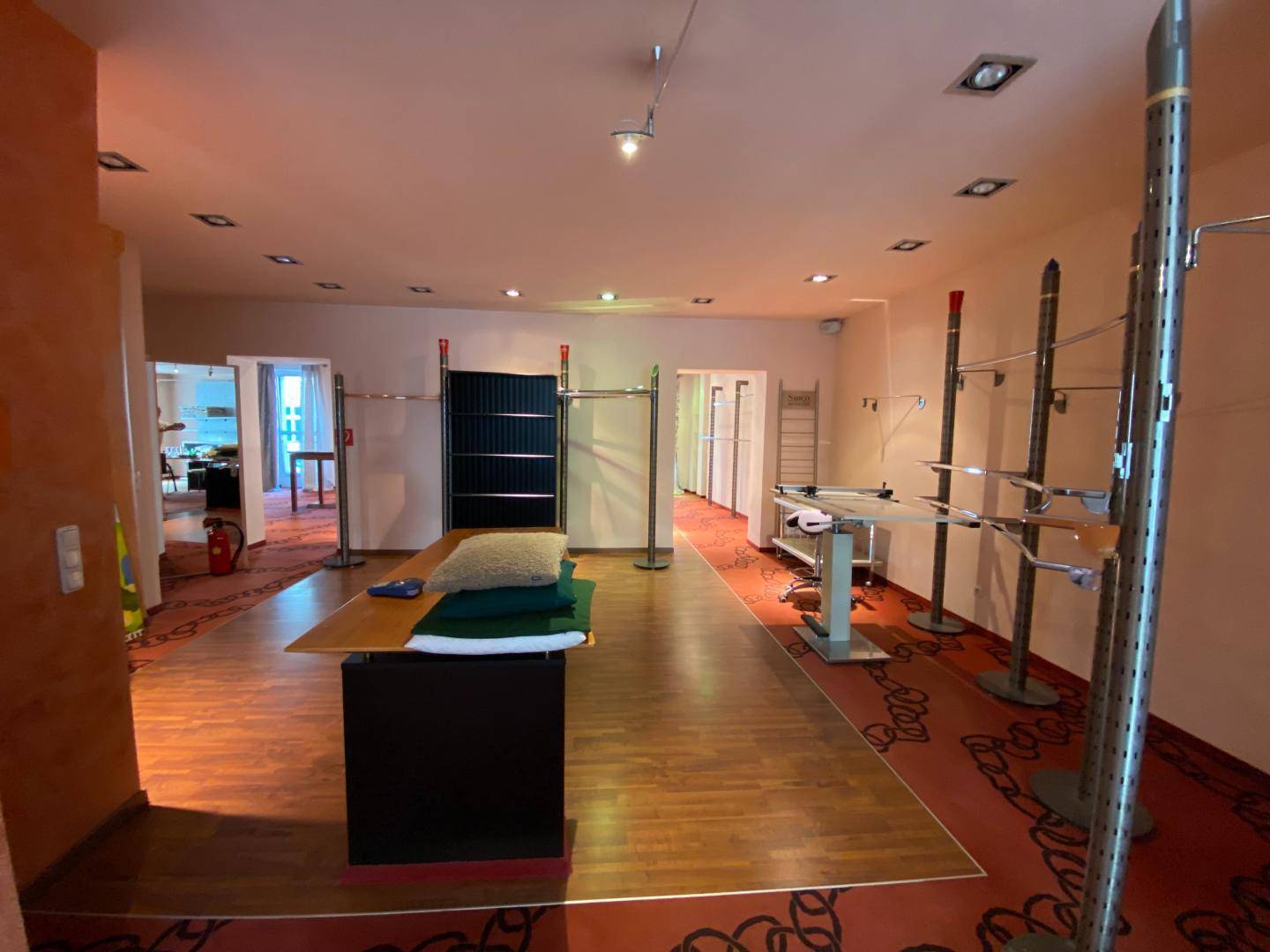 Großer Verkaufsraum mit flexiblen Kleiderständern, Holzboden und Teppichbereich.