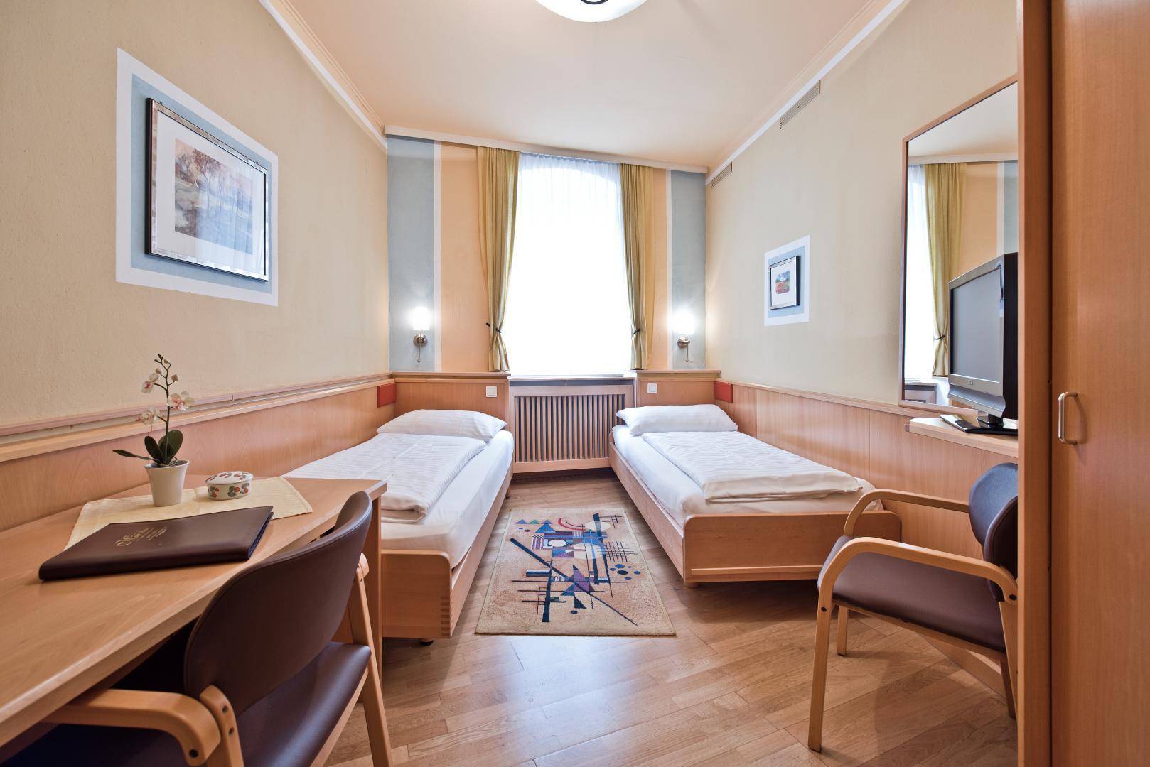 Helles Schlafzimmer mit zwei Einzelbetten, Schreibtisch und Holzmöbeln in freundlicher Atmosphäre.