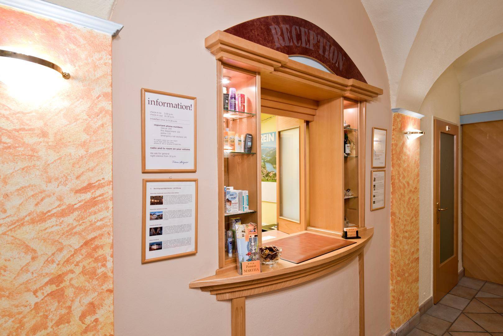 Empfangsbereich mit Holztheke, Informationsmaterial und dekorativen Wandleuchten in warmen Tönen.