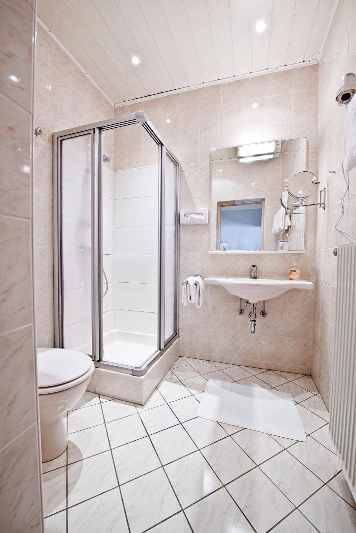 Helles Badezimmer mit Duschkabine, WC, Waschbecken und beigefarbenen Fliesen an Wänden und Boden.