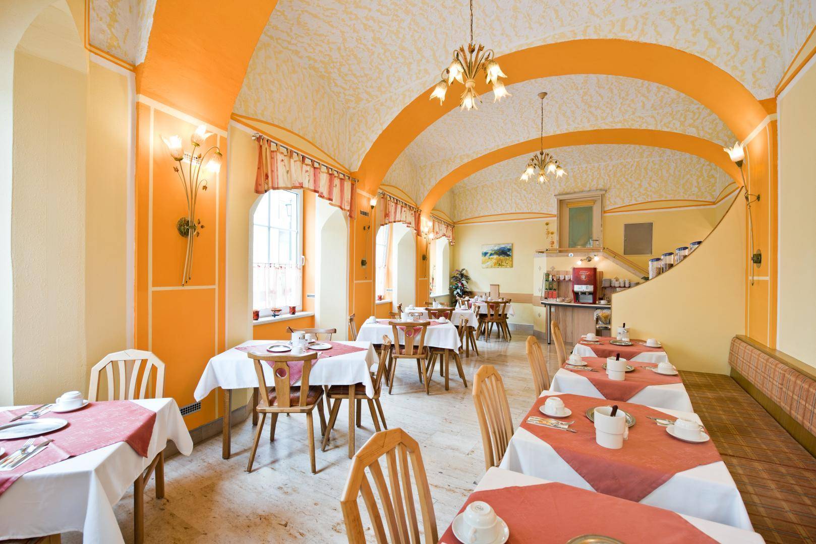 Geräumiger Speisesaal mit Gewölbedecken, Buffetbereich und Treppenaufgang in warmer Farbgebung.