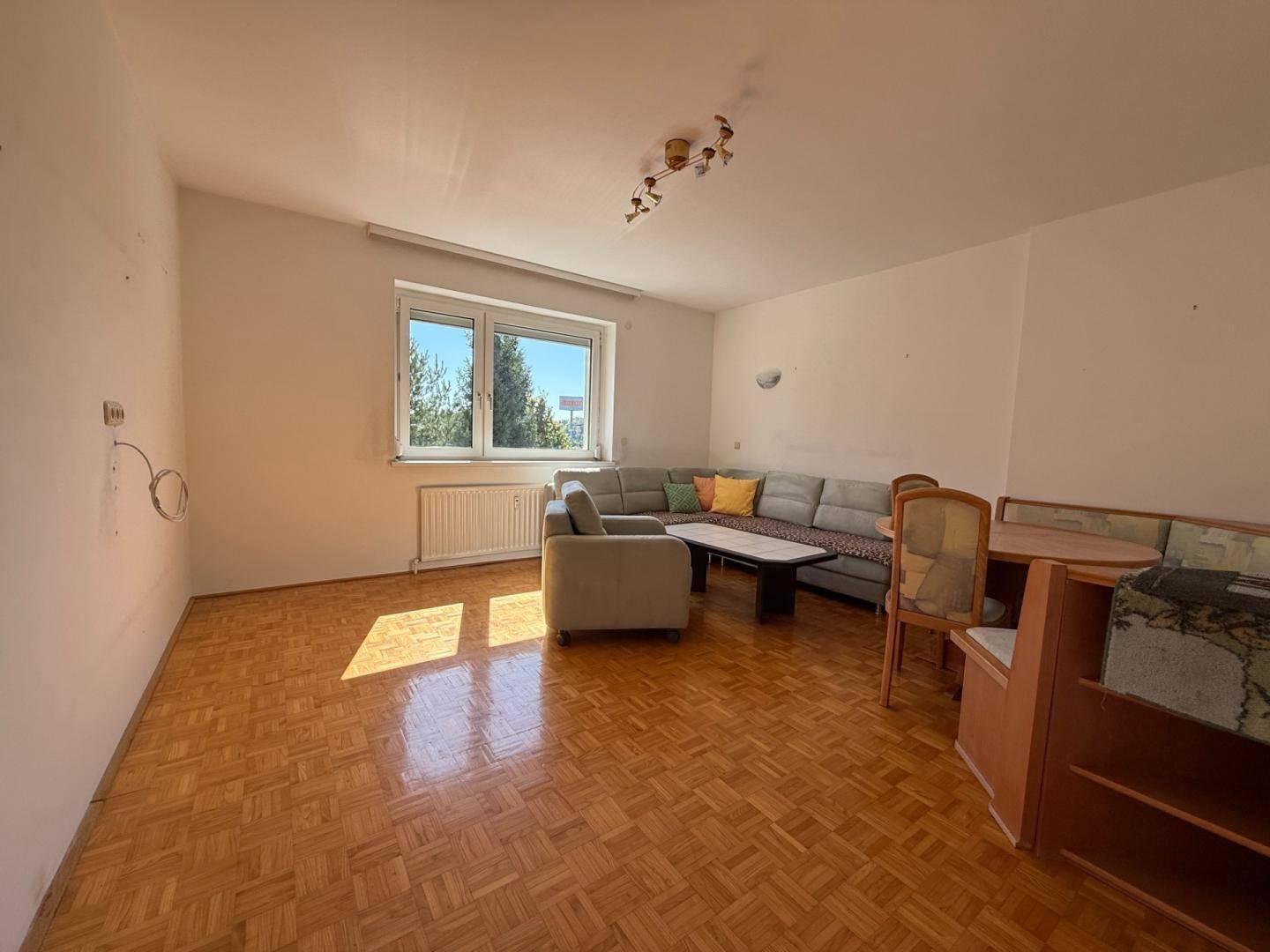 Geräumiges Wohnzimmer mit Parkettboden, großem Fenster und gemütlicher Eckcouch.