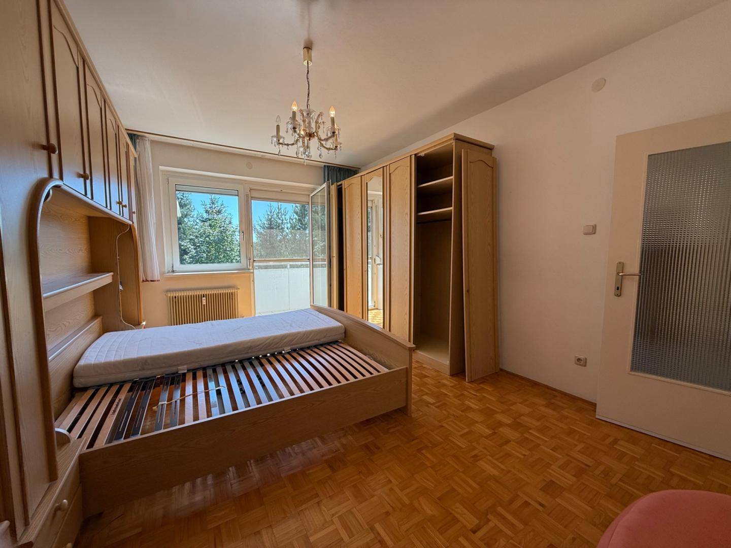 Schlafzimmer mit Parkettboden, großem Fenster und Einbauschränken in hellem Holzton.