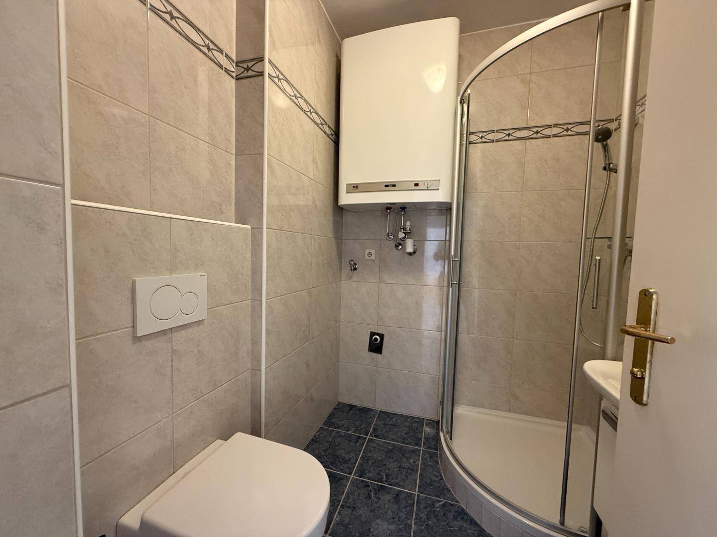 Kleines Badezimmer mit Duschkabine, WC und hellen Fliesen an Wänden und Boden.