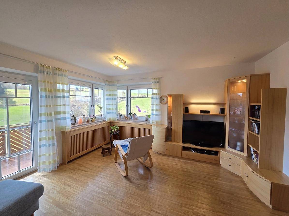 Helles Wohnzimmer mit Holzboden, großen Fenstern und direktem Zugang zum Balkon.