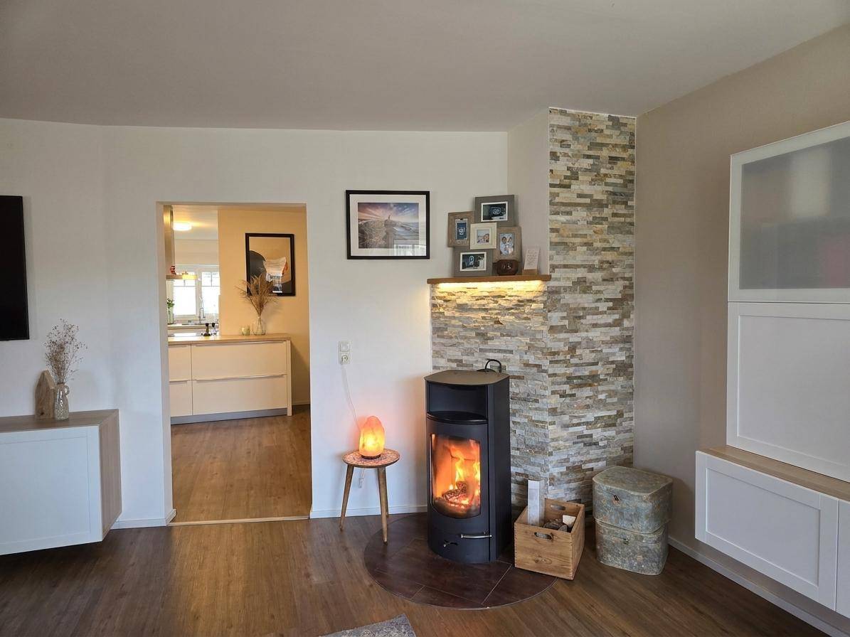 Wohnzimmer mit modernem Holzofen, Steinwandverkleidung und Zugang zur Küche.