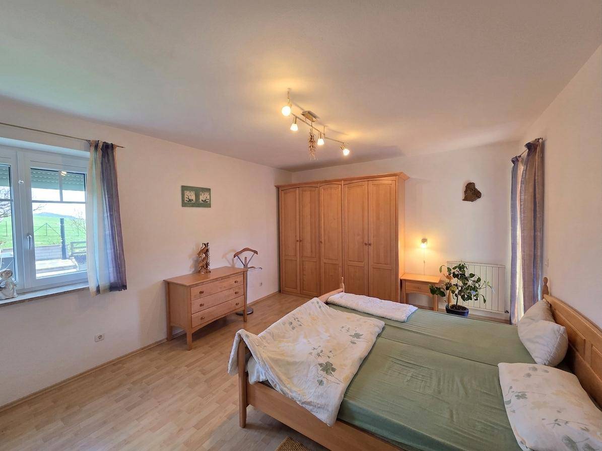 Schlafzimmer mit Holzbett, Kleiderschrank und Blick ins Grüne durch das Fenster.