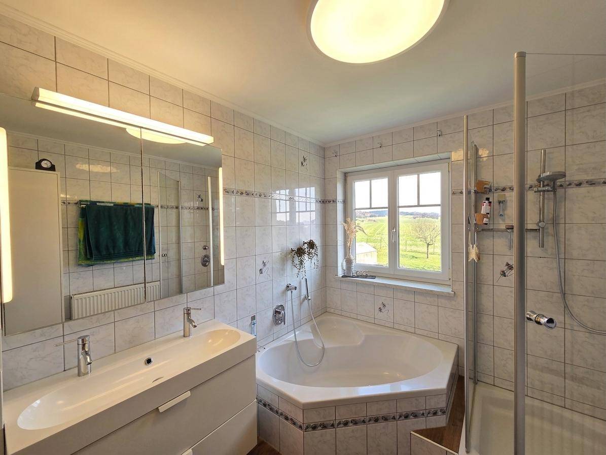 Helles Badezimmer mit Eckbadewanne, Dusche, Doppelwaschbecken und Fenster mit Ausblick.