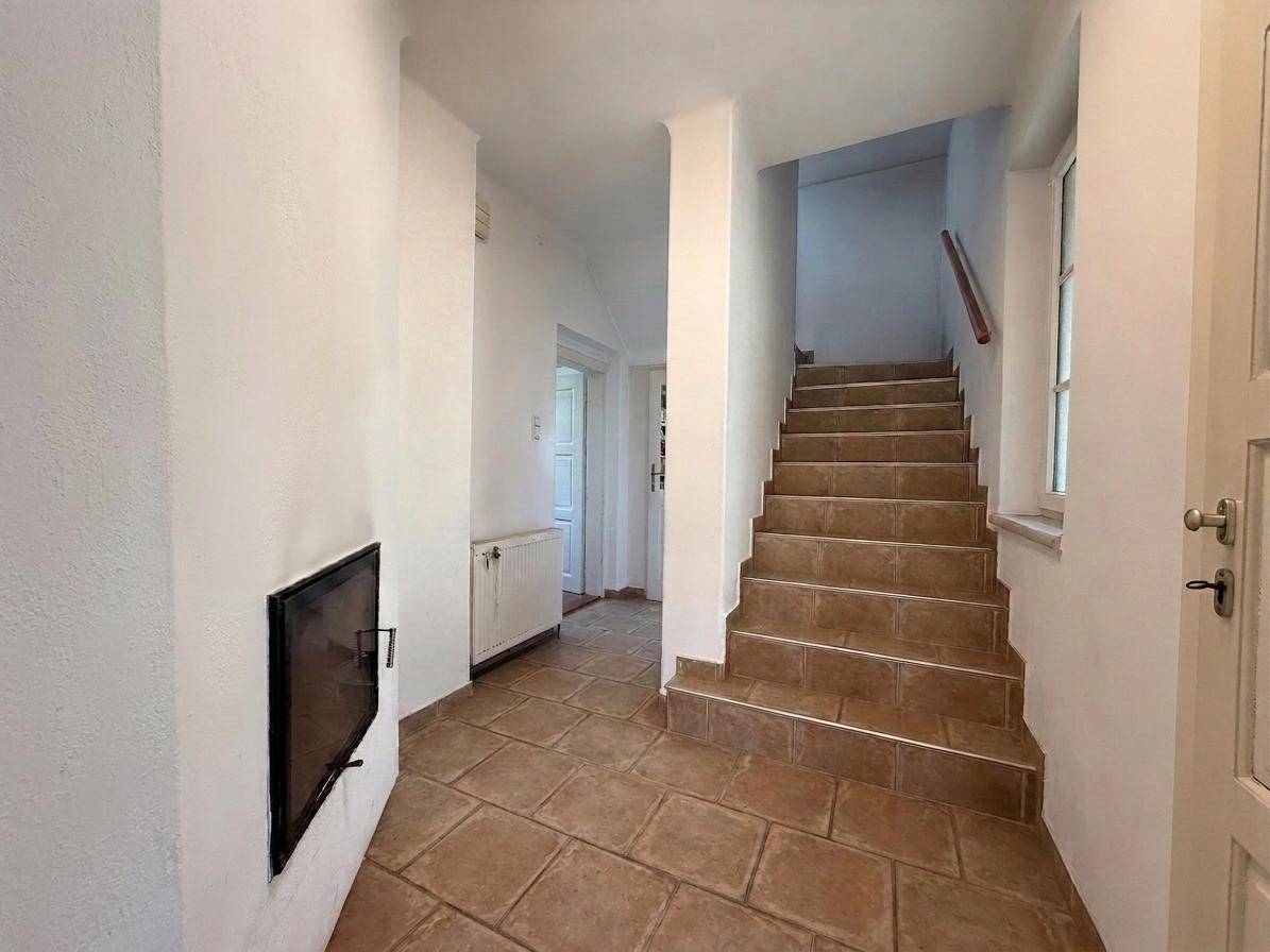 Heller Flur mit gefliestem Boden, Treppe und einem eingebauten Kamin.