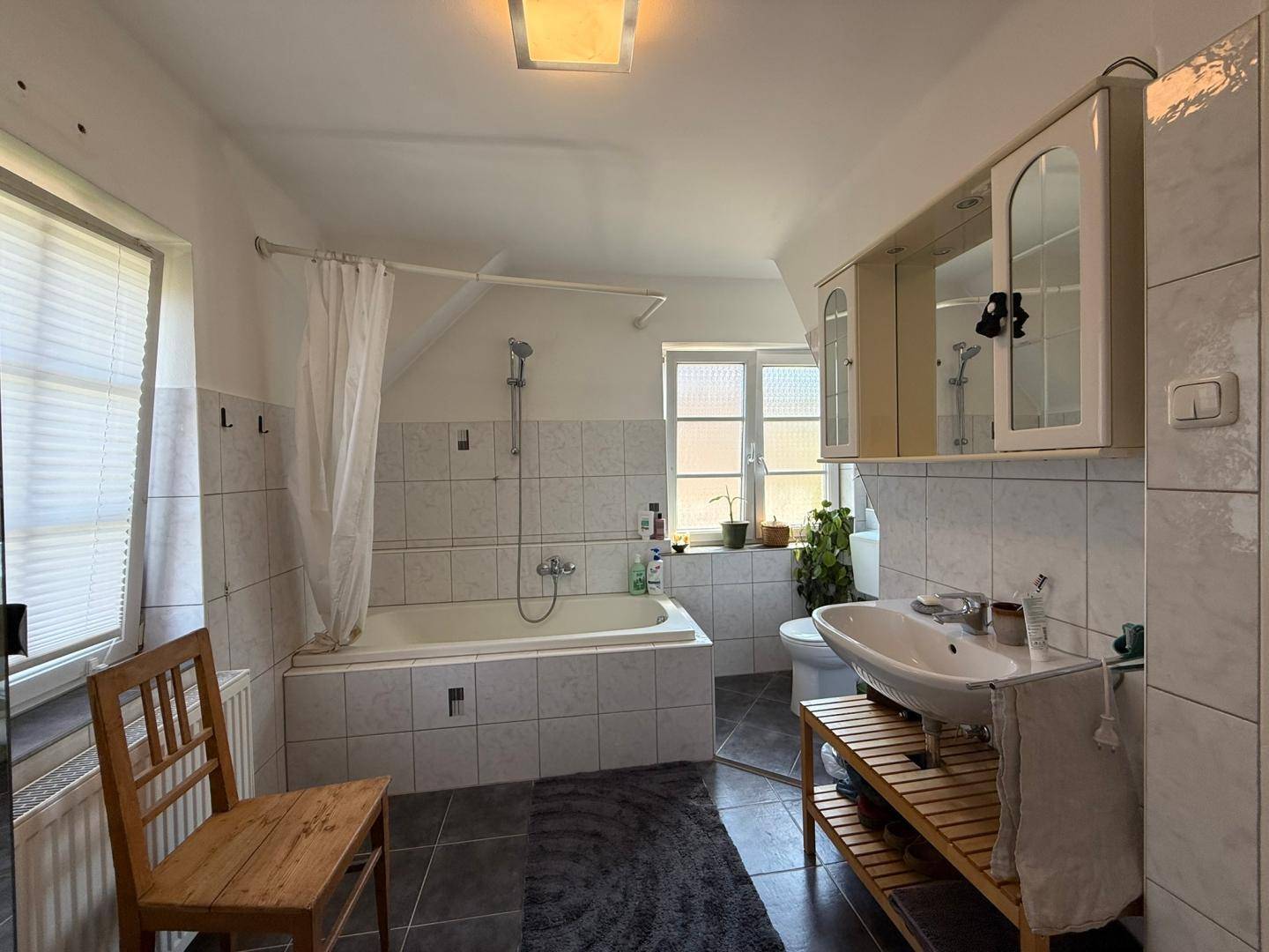 Gefliestes Badezimmer mit Badewanne, Waschbecken und Spiegelschrank unter Dachschräge.