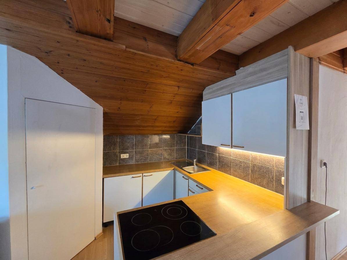 Dachgeschossküche mit Holzbalkendecke, Einbaugeräten und schrägen Wänden.