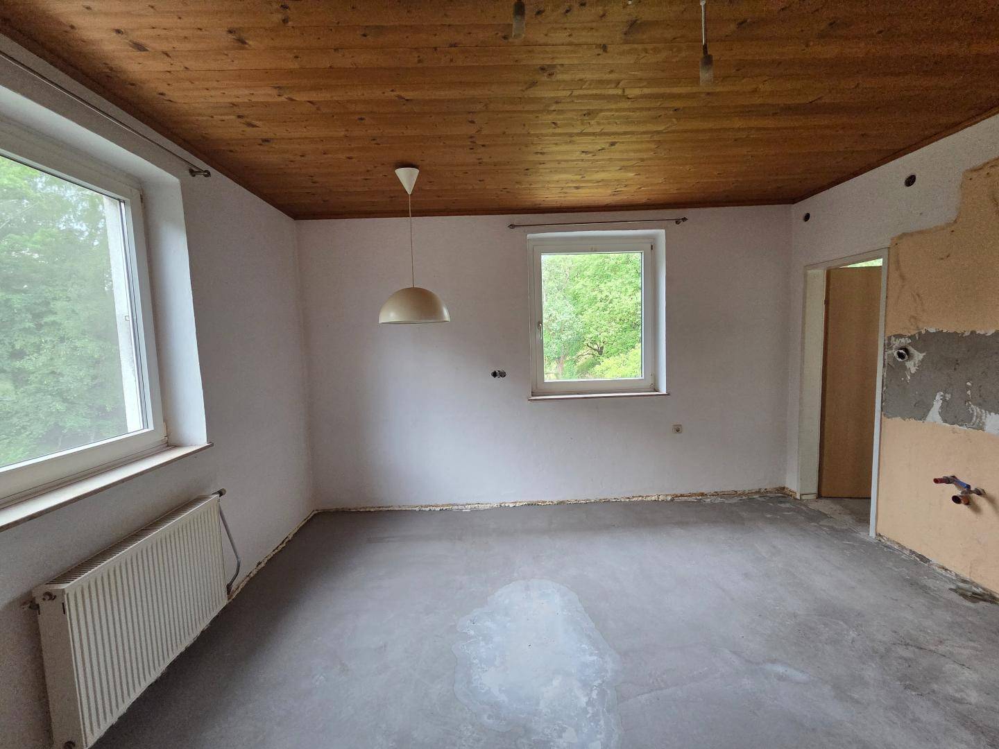 Unfertiger Raum mit Holzbalkendecke und Estrichboden, bereit für den Ausbau.