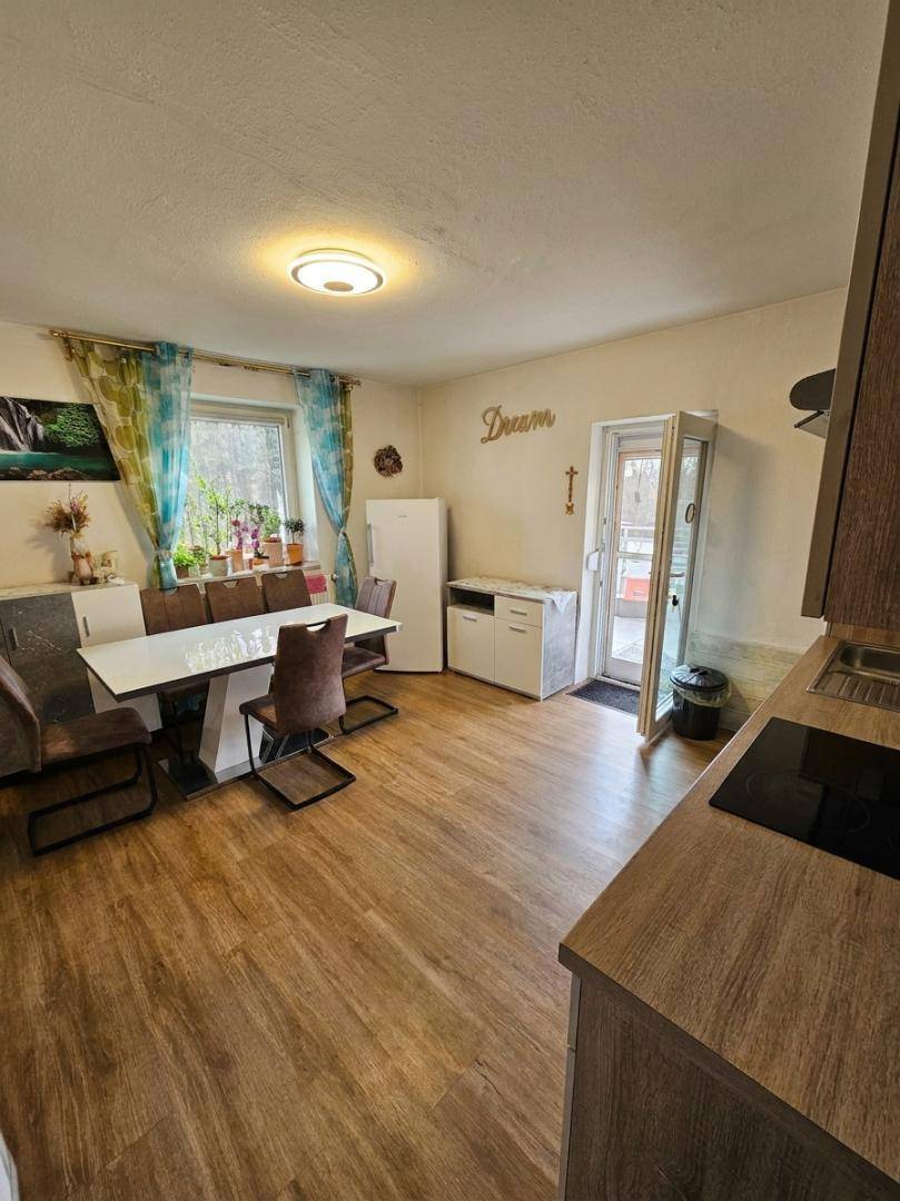 Offene Wohnküche mit Essbereich, Laminatboden und Zugang zu einem Balkon.