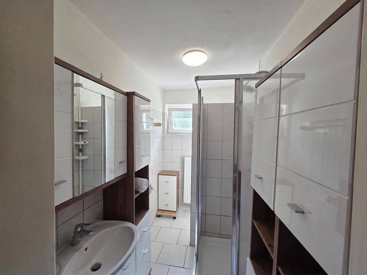 Modernes Badezimmer mit Dusche, Waschtisch und Spiegelschrank, hell gefliest.