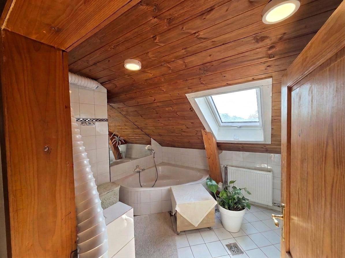 Badezimmer im Dachgeschoss mit Badewanne, Holzbalkendecke und Dachfenster.
